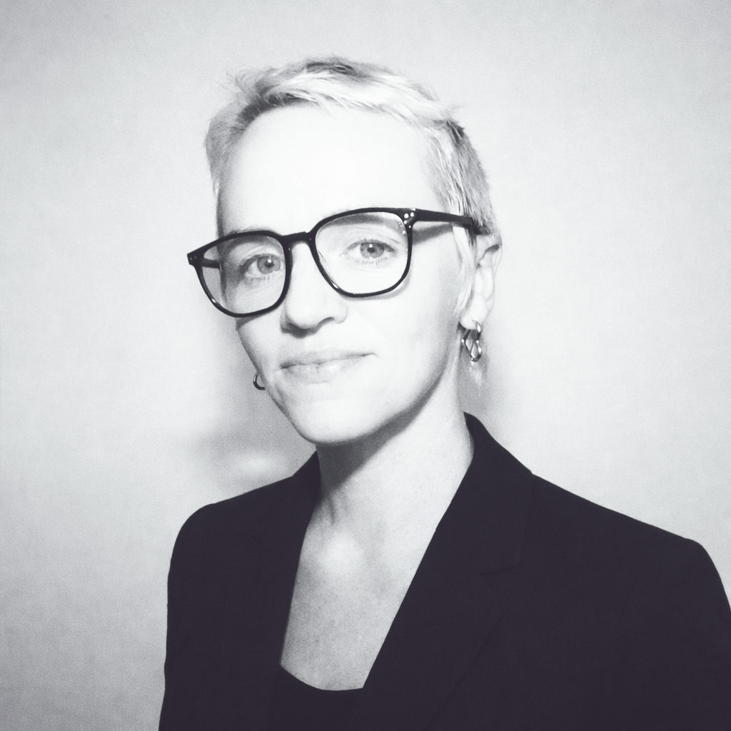 Portrait of Leia Sidery, founder of The Art of Wall, wearing black blazer and glasses against a neutral background