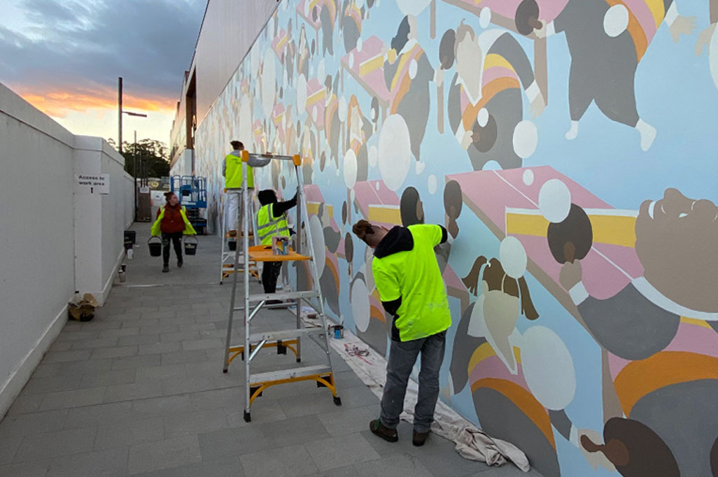 Painters working on the Between Mountains mural, adding vibrant colors to the large-scale design in the atriumof the building.